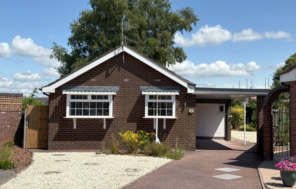 A sunny exterior of a single-story, dark brick detached bungalow on Waveney Grove