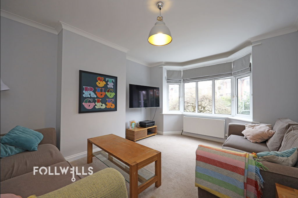Bright living room with bay window, neutral décor, wall-mounted TV and comfortable seating.