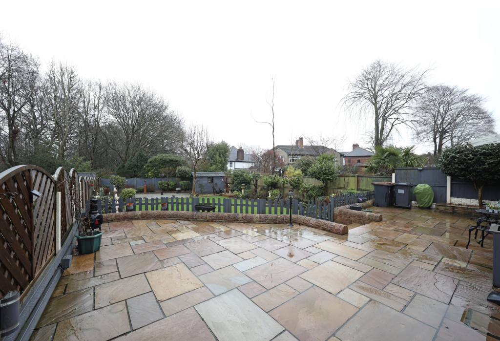 Spacious paved patio leading to a private garden with lawn, fencing and mature trees.