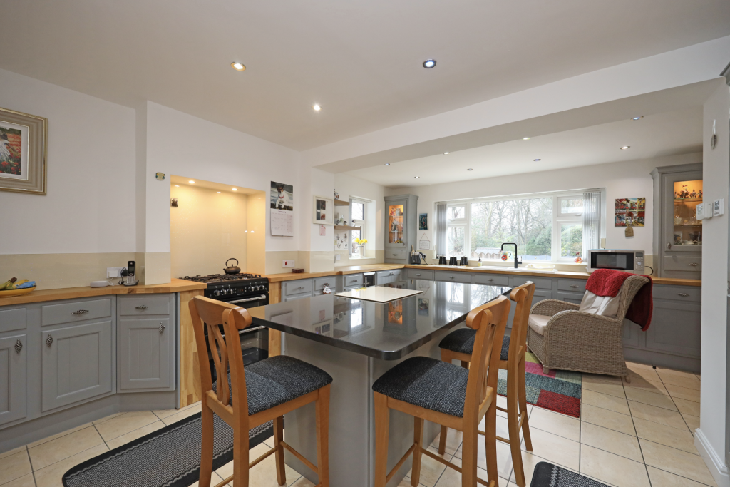 Open-plan kitchen with central island, grey cabinetry, wooden worktops and large windows overlooking the garden.