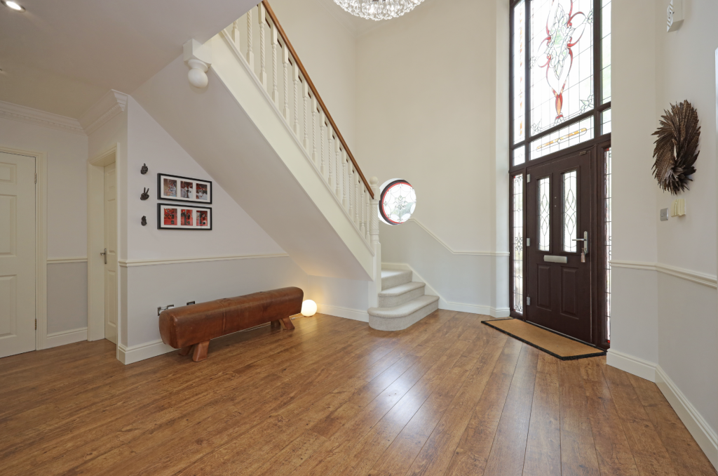 Spacious entrance hallway with wooden flooring, staircase with white balustrade, stained glass front door, and modern lighting.