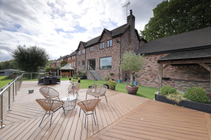 Large rear decked terrace with outdoor seating, landscaped garden, and brick-built home overlooking greenery.