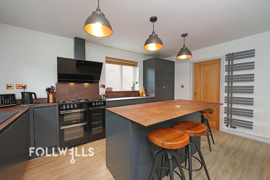Modern fitted kitchen with dark cabinets, pendant lighting, island seating and wood-effect worktops.