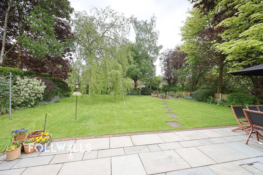 Large rear garden with lawn, patio area, mature trees, shrubs and outdoor seating.