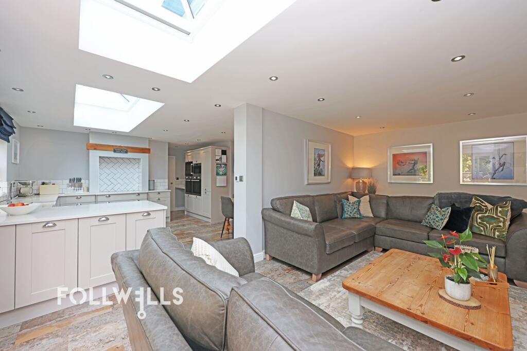 Open-plan kitchen and living area with skylights, grey sofas, white cabinets and a wooden coffee table.