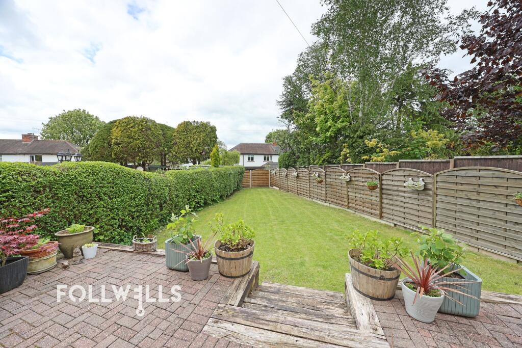 Rear garden with a patio, lawn, potted plants, hedges and timber fencing.